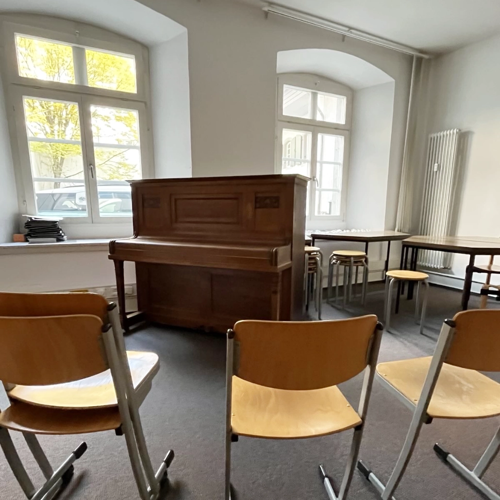 Klavier Faure-Raum Pilgerstab In einem Probensaal stehen leere Stühle um ein hohes Klavier herum. Dahinter sind zwei große Fenster.