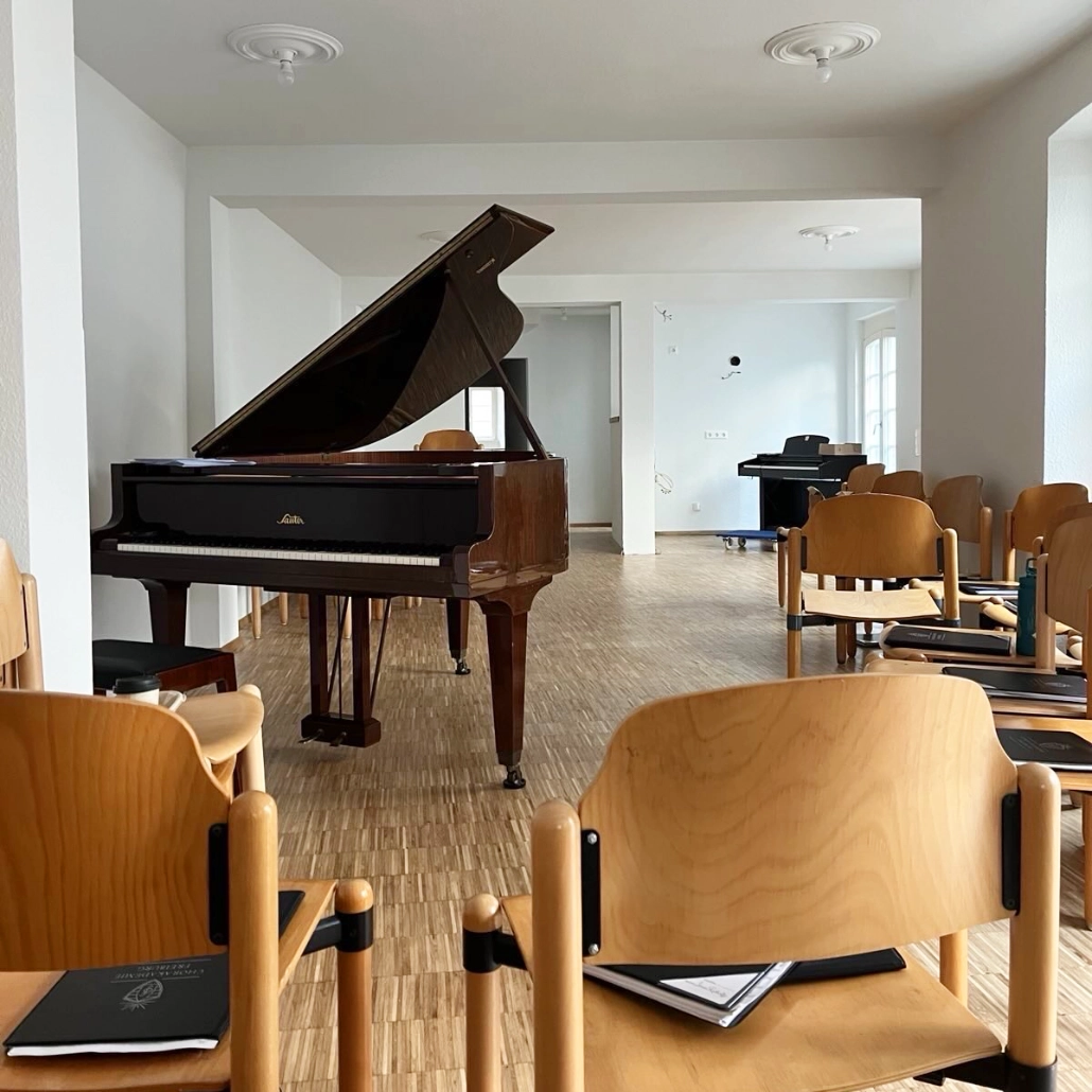 Klavier Flügel Bach-Raum Pilgerstab In einem großen Probensaal steht ein offener Flügel. Darum sind viele Stühle aus Holz aufgestellt.