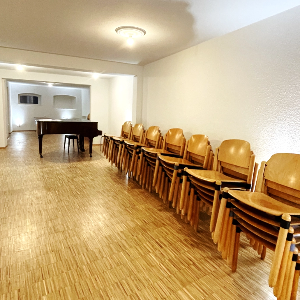 Pilgerstab Probenraum Bach-Raum Stühle 1030 x 1030 In einem großen Probensaal stehen viele Stühle aufeineander gestapelt am Rand. In der Mitte steht ein brauner Klavieflügel