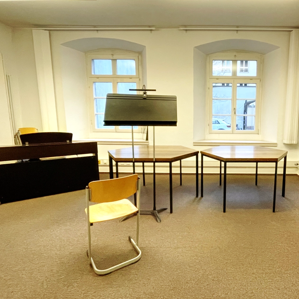 Pilgerstab Probenraum Faure-Raum e-piano 1030 x 1030 In einem Probensaal ein Stuhl, zwei Tische, ein Dirigentenpult und ein E-Piano