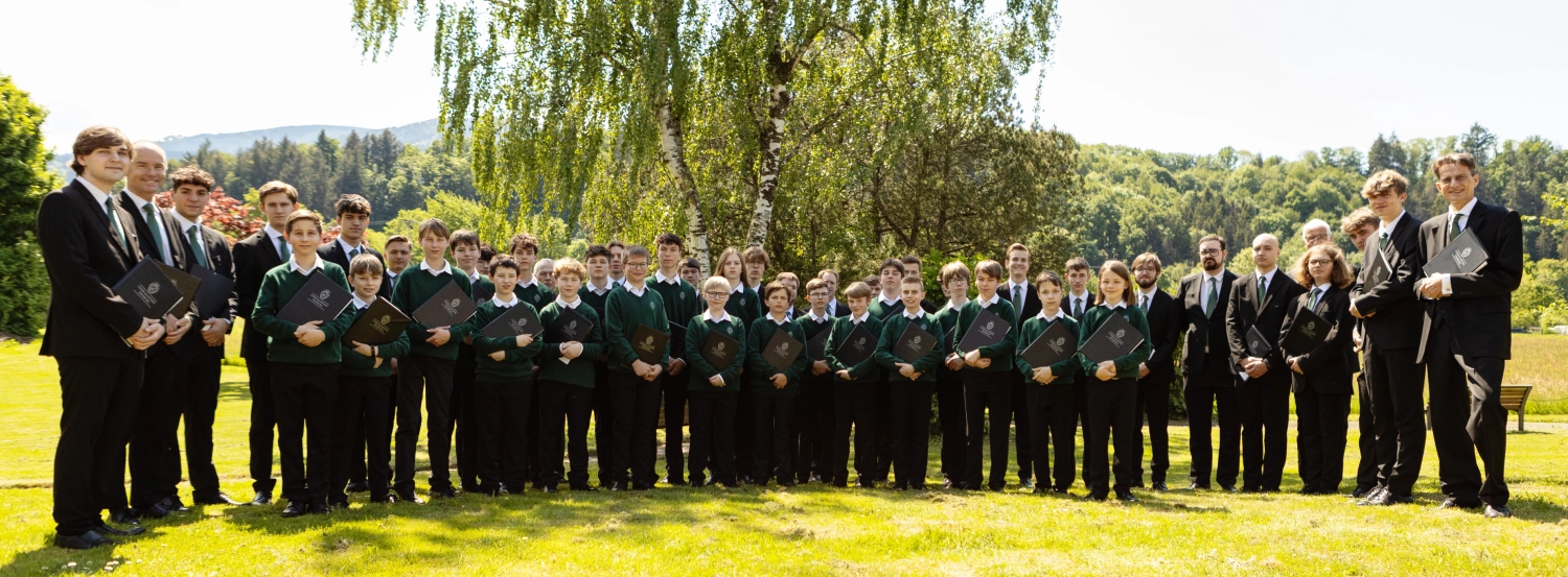 Teaser Knabenchor Konzert Etwa 80 Jungs und der Chorleiter stehen nebeneinander in einem Park