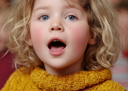 Im Vordergrund steht ein Mädchen das singt. Im Hintergrund stehen weitere musizierende Kinder